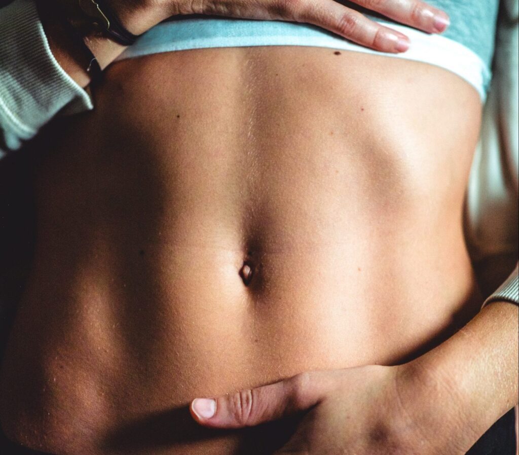 A woman with her hands on the top and bottom of her bare stomach